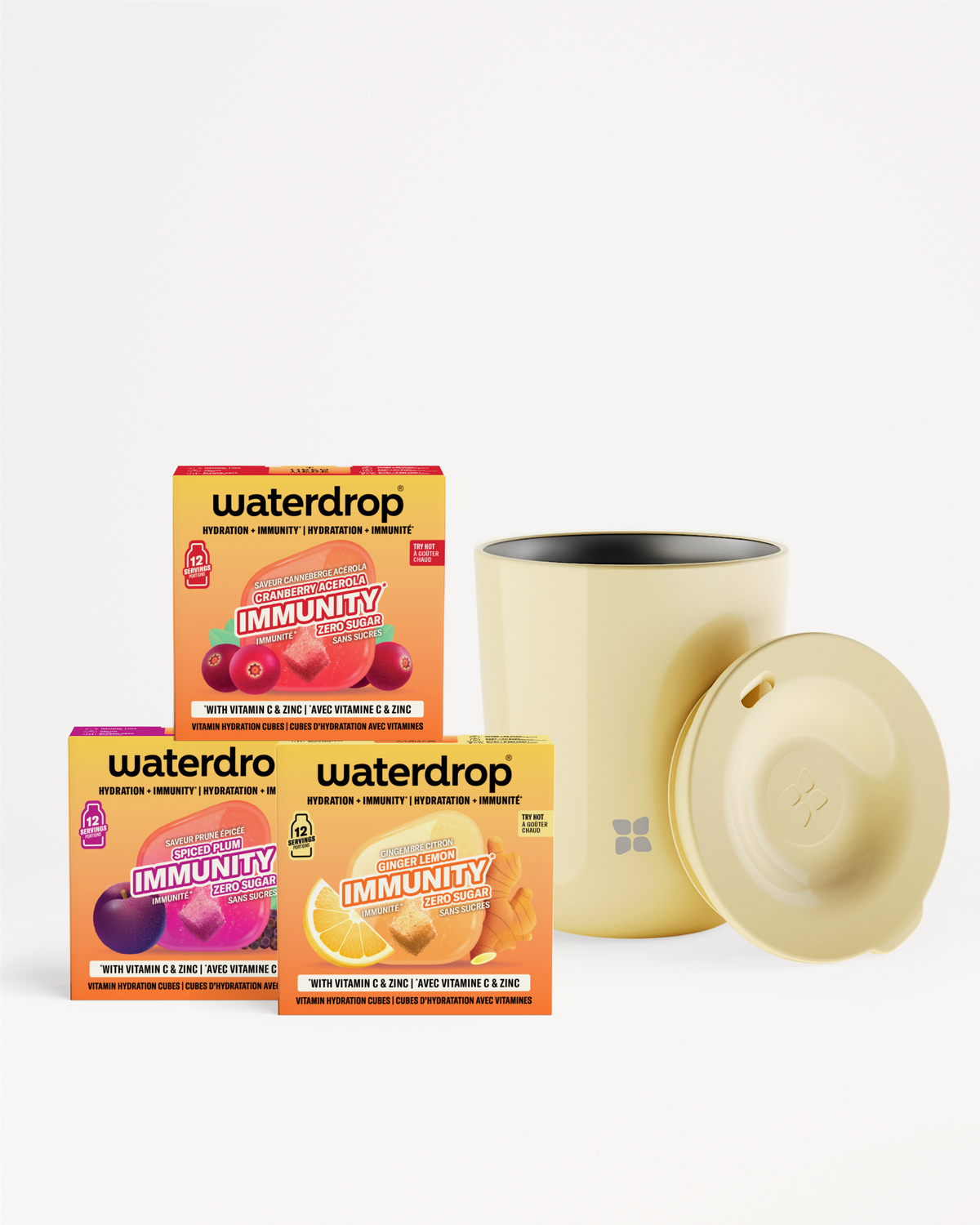 Drei Vitamin-Getränkepackungen und eine beigefarbene Tasse mit Deckel vor weißem Hintergrund.