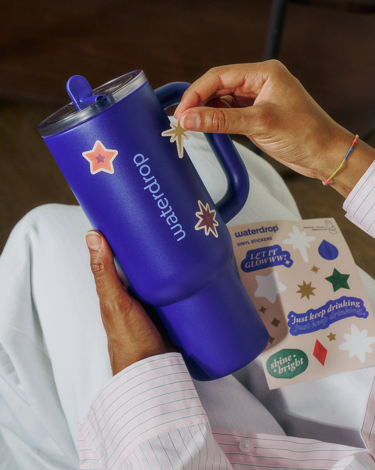 Adventskalender Large: Person verziert blauen waterdrop®-Tumbler mit Leuchtstickern.
