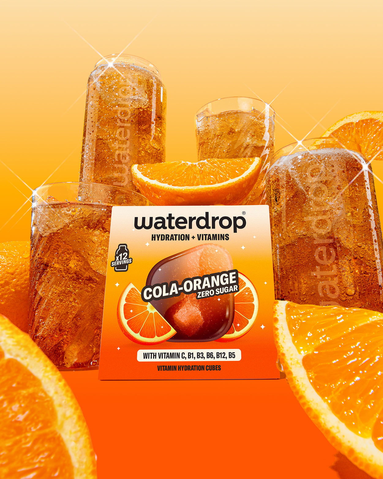 COLA ORANGE Vitamincubes in Box mit sprudelndem Getränk und Orangenstücken.