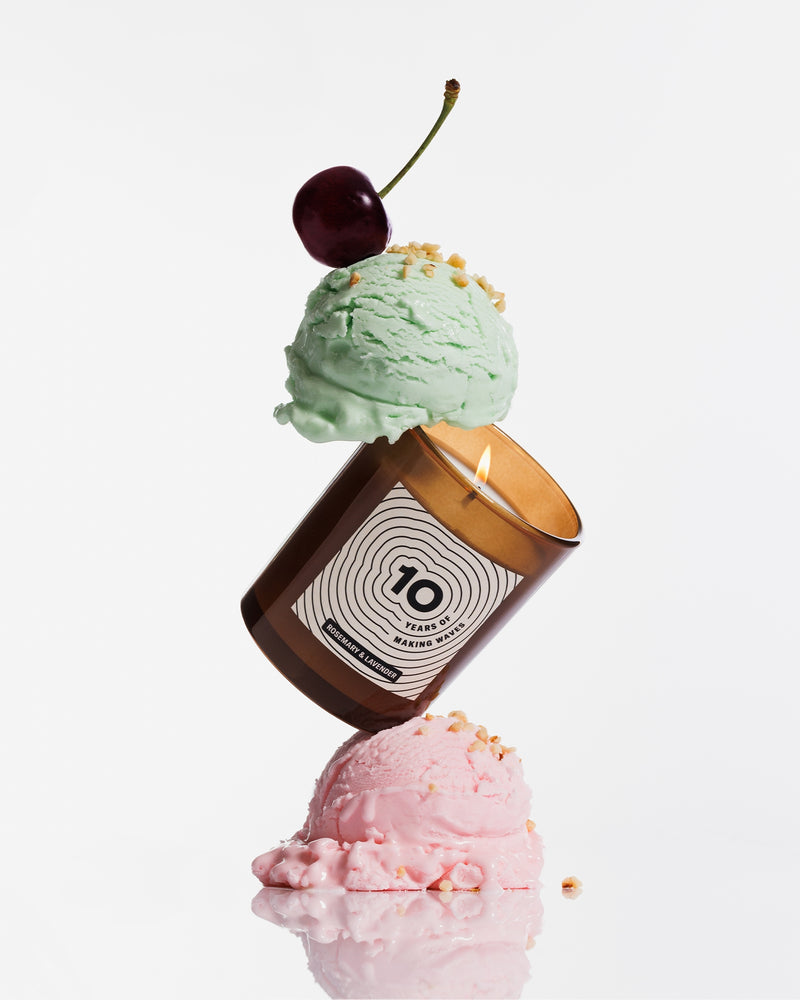 Braune Kerze, die zwischen zwei Pastell-Eiskugeln balanciert ist und mit einer Kirsche dekoriert ist.