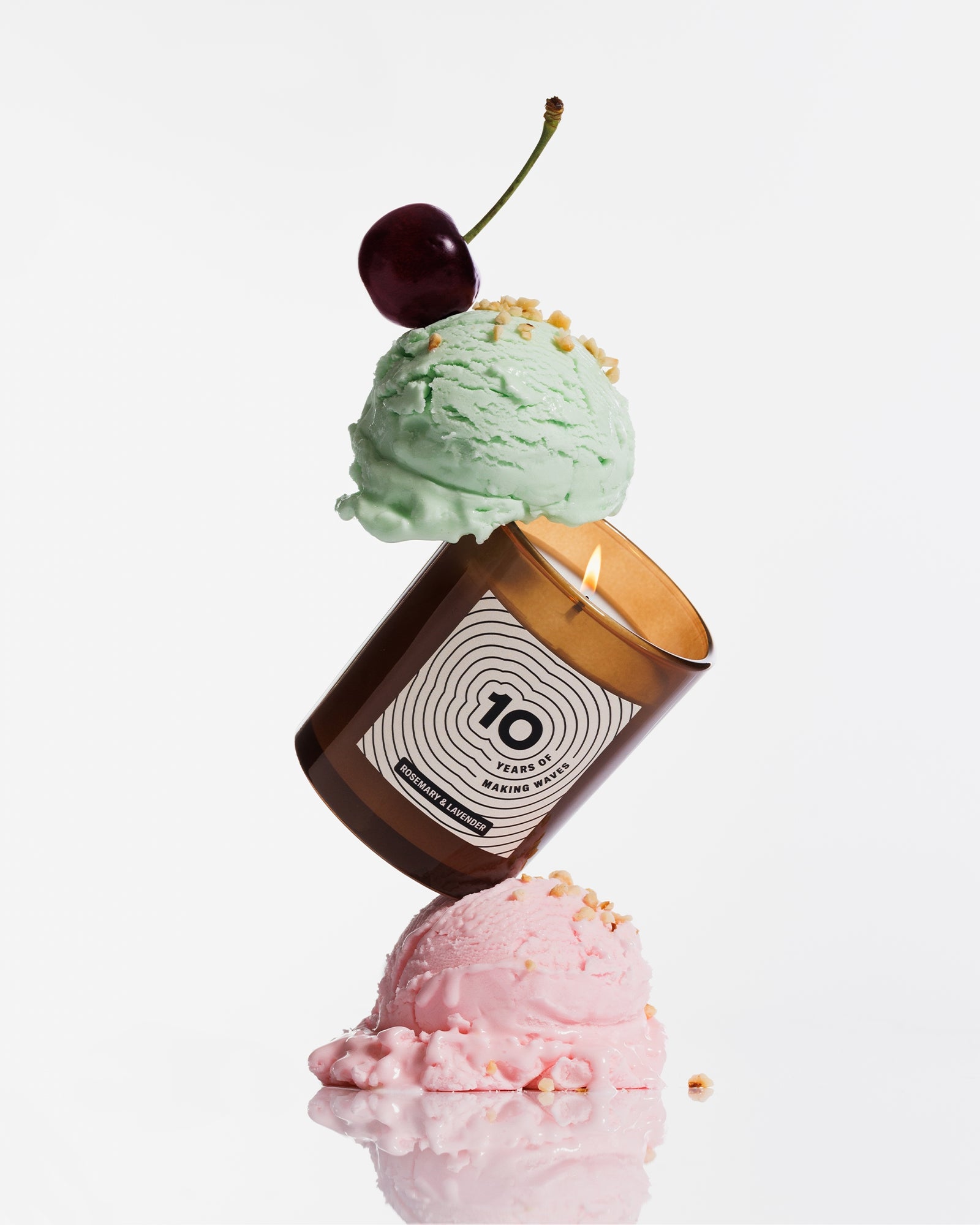 Braune Kerze, die zwischen zwei Pastell-Eiskugeln balanciert ist und mit einer Kirsche dekoriert ist.