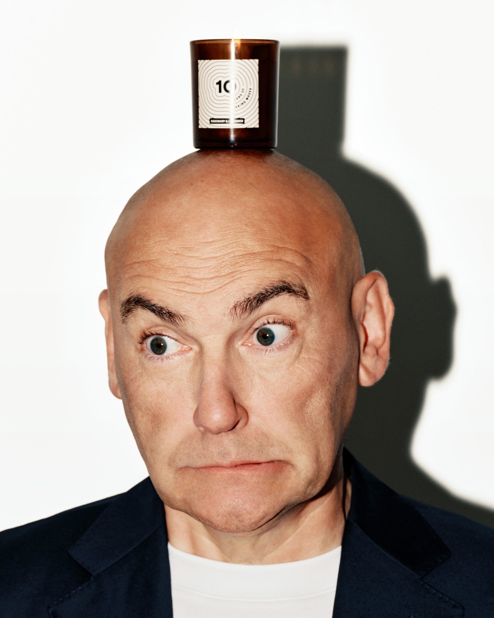 Glatter Mann in dunklem Blazer mit einer kleinen kupfernen Flasche balanciert auf dem Kopf.