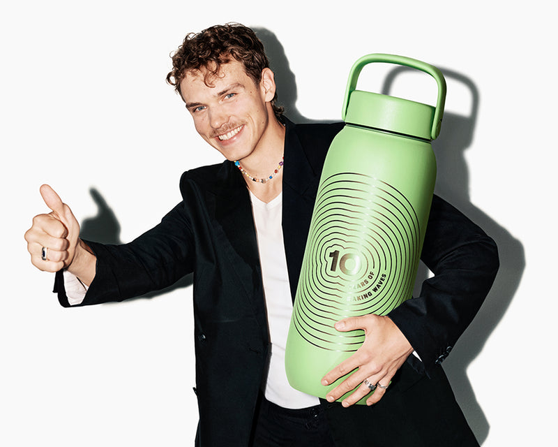 Lächelnder Mann im Sakko hält eine große grüne wiederverwendbare Trinkflasche mit Griff und zeigt Daumen hoch.