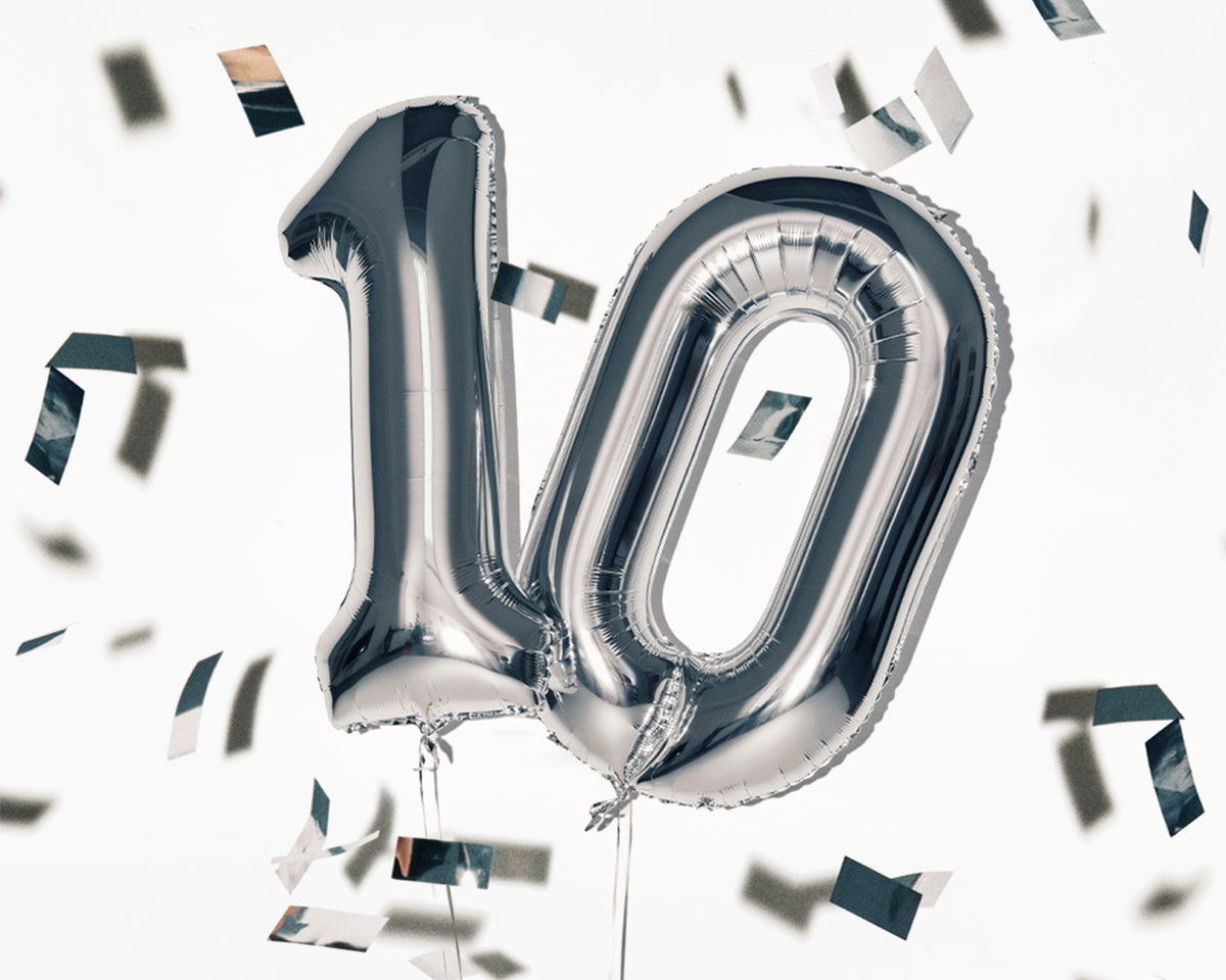 Silberne Folienballons in der Form der Zahl 10 mit verstreutem Konfetti.