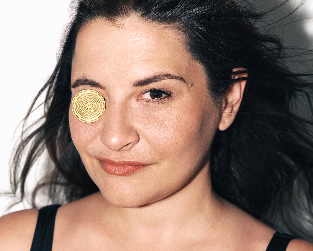Nahaufnahme einer Frau mit rundem goldenen Kosmetikpflaster über einem Auge.