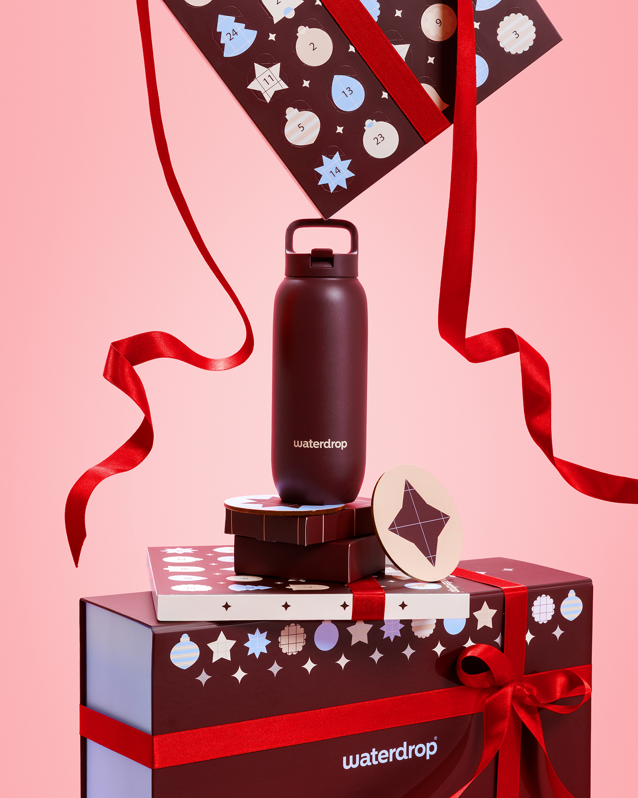 Dunkle Flasche auf Geschenkboxen mit roten Schleifen vor rosa Hintergrund.