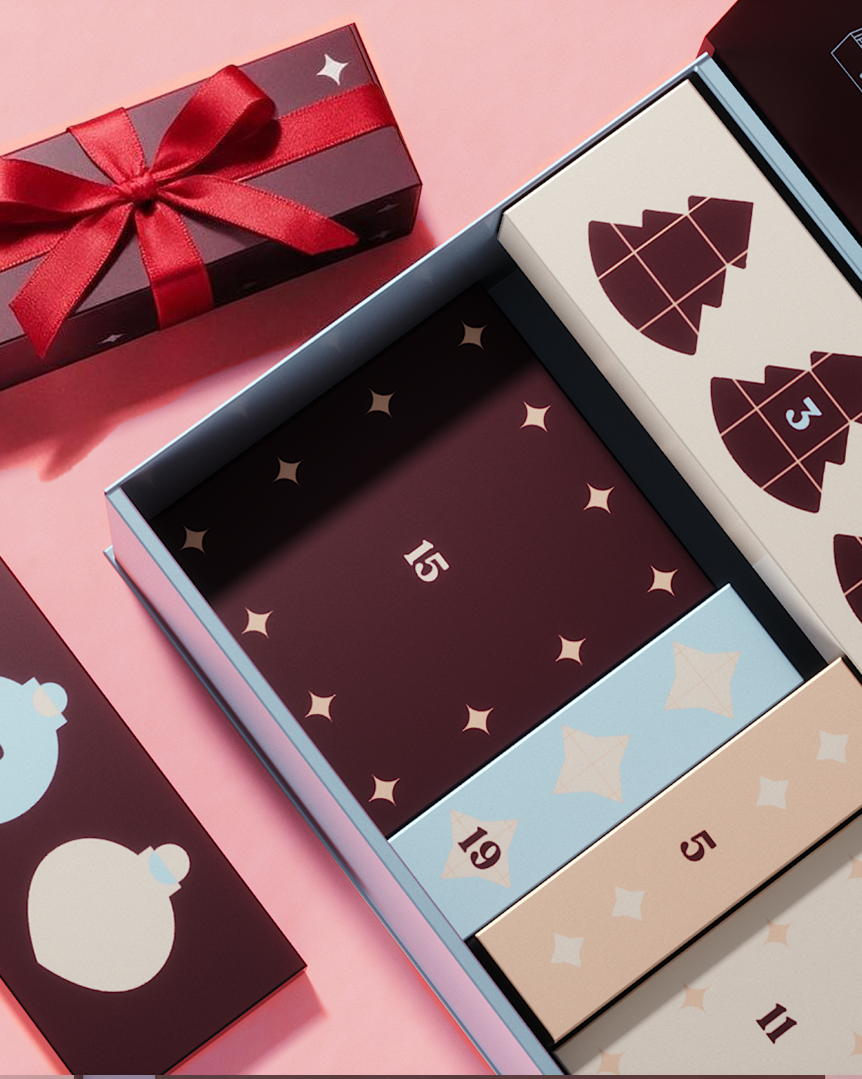 Adventskalender mit dekorativen Feldern und roter Geschenkschachtel vor rosa Hintergrund.
