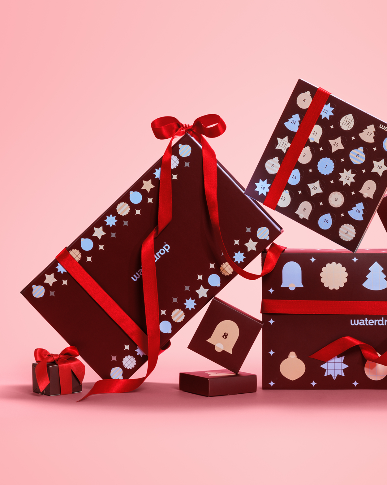 Zusammengebundene Geschenkkartons mit roten Schleifen und festlichen Mustern auf rosa Hintergrund.