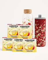 Vier Waterdrop-Boxen für Hydration und Vitamine, eine klare Flasche mit holzner Kappe und ein roter Becher mit Muster.