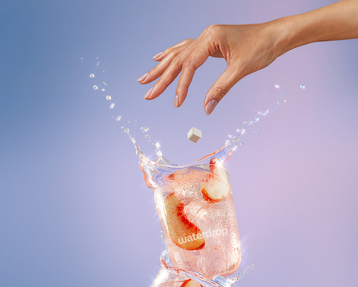 Hand fällt einen kleinen Eiswürfel in ein Glas Wasser mit Eis und erzeugt einen Spritzer.