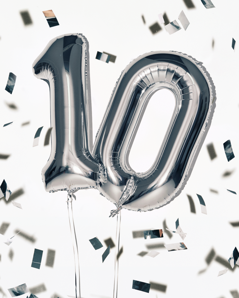 Silberne Folienballons in der Form der Zahl 100 mit Bändern, umgeben von Konfetti.