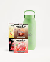 Drei Waterdrop-Geschmacksprobenboxen vor einer grünen wiederverwendbaren Flasche.
