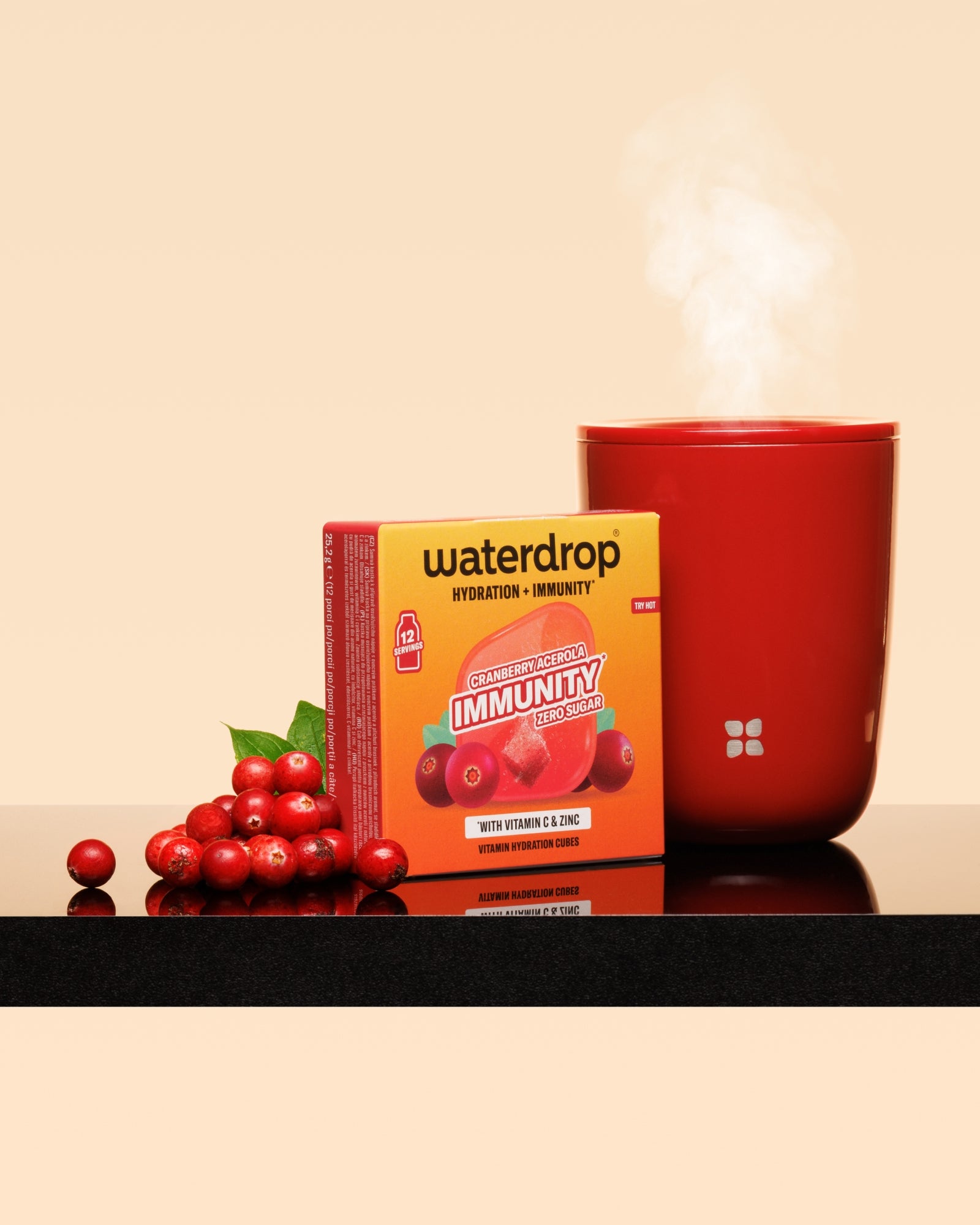 Roter dampfender Becher neben einer roten Box und einer Cranberry-Garnitur auf einer glänzenden Oberfläche.