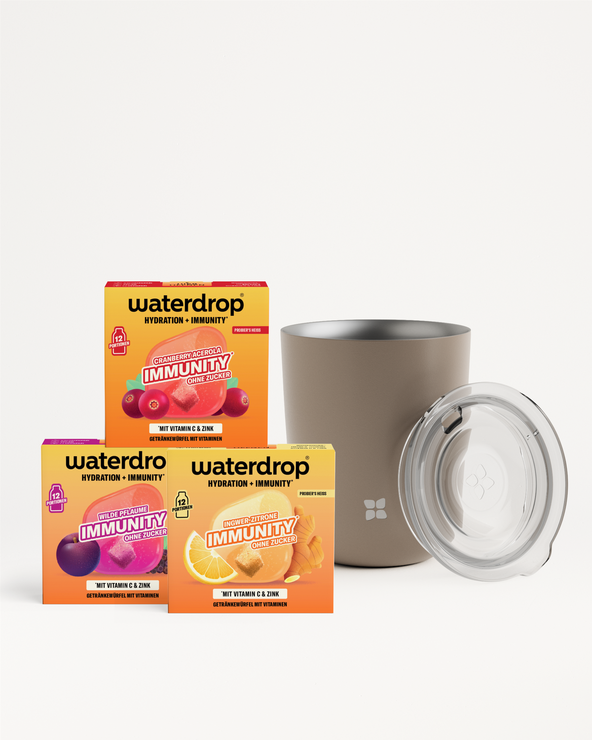 Drei bunte Vitaminboxen neben einer beigen Tasse mit transparentem Deckel vor hellem Hintergrund.
