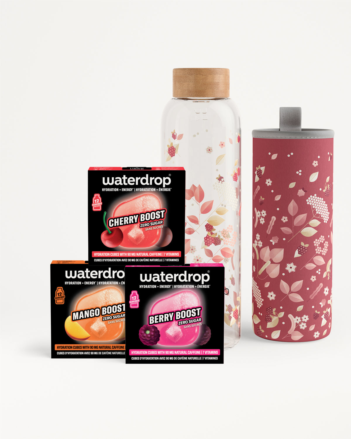 Sortiment aus drei Flavor-Boost-Portionen neben einer klaren Glasflasche mit Holzdeckel und einem hohen pinkfarbenen, blumenmuster Tumbler.