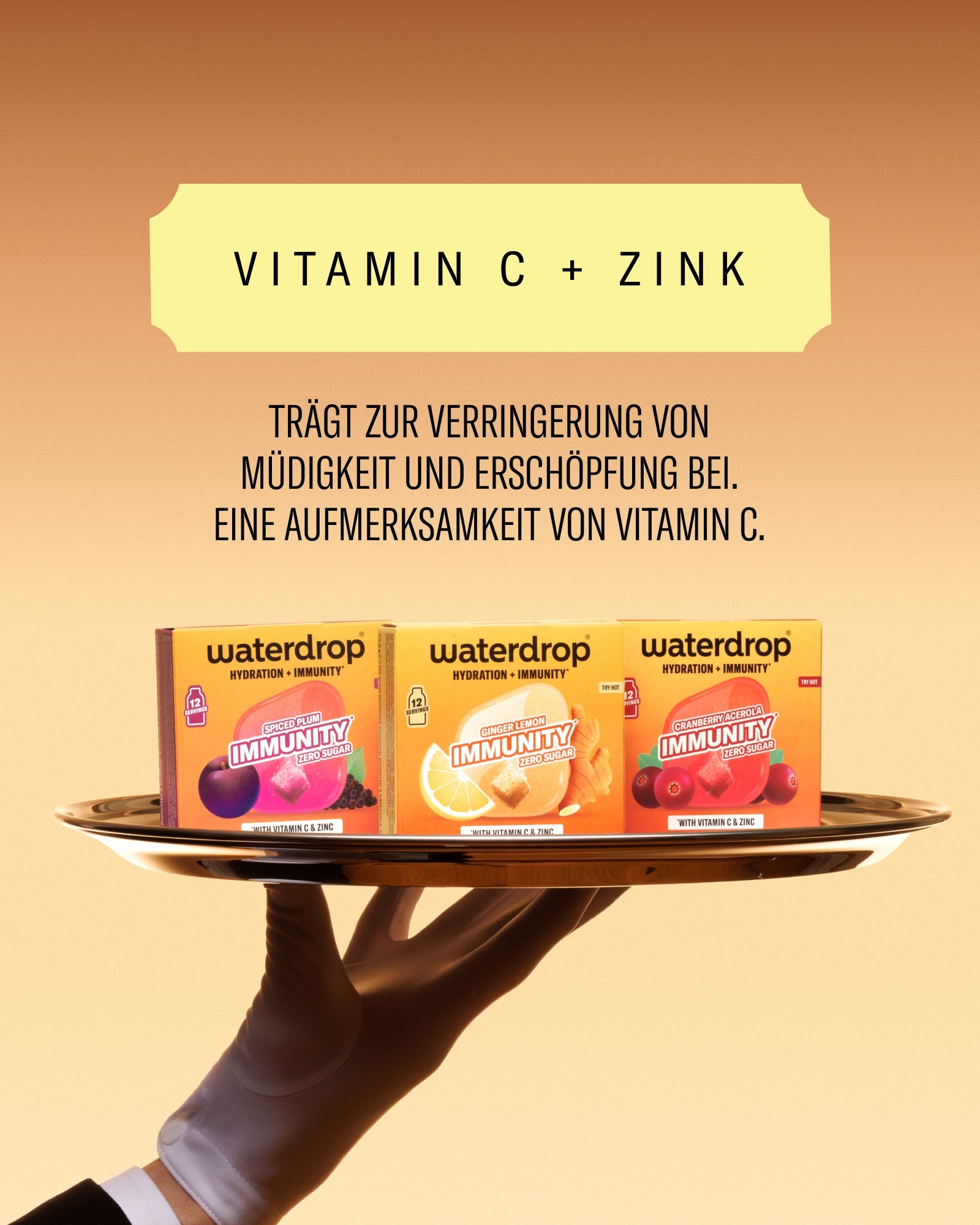 Drei Waterdrop Vitamin-C+Zink-Boxen auf einem Teller, gehalten von einer Hand mit Handschuh, vor orangem Verlauf.