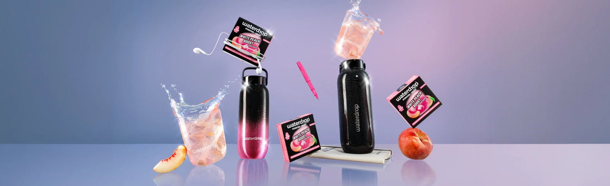 Eine Kollektion schwarzer Flaschen mit pinker Flüssigkeit und kleinen Produktverpackungen, verstreut auf einer pastellblauen Oberfläche.