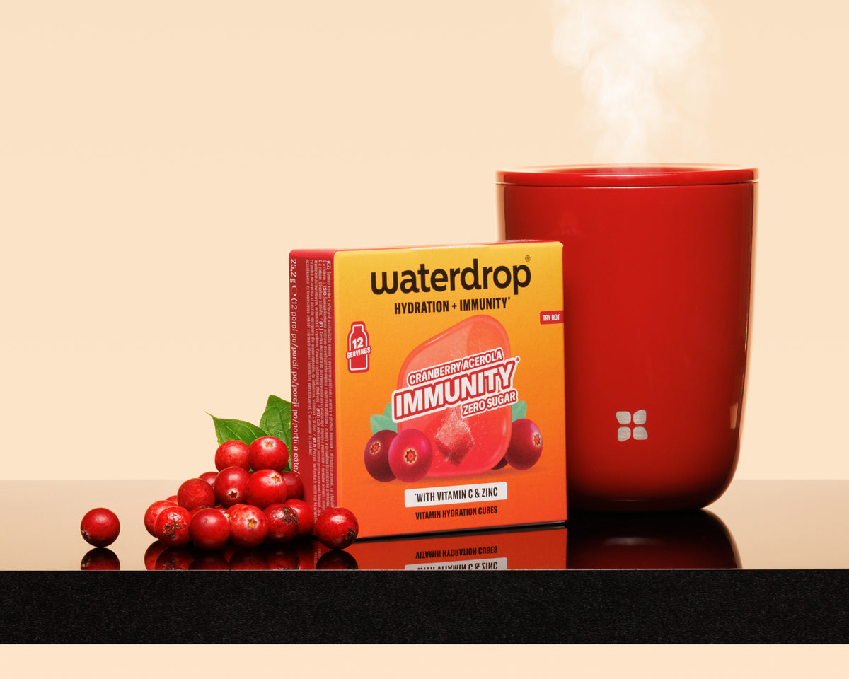 Orangene Box neben einer dampfenden roten Tasse und einem Bündel roter Beeren auf einer reflektierenden Oberfläche.