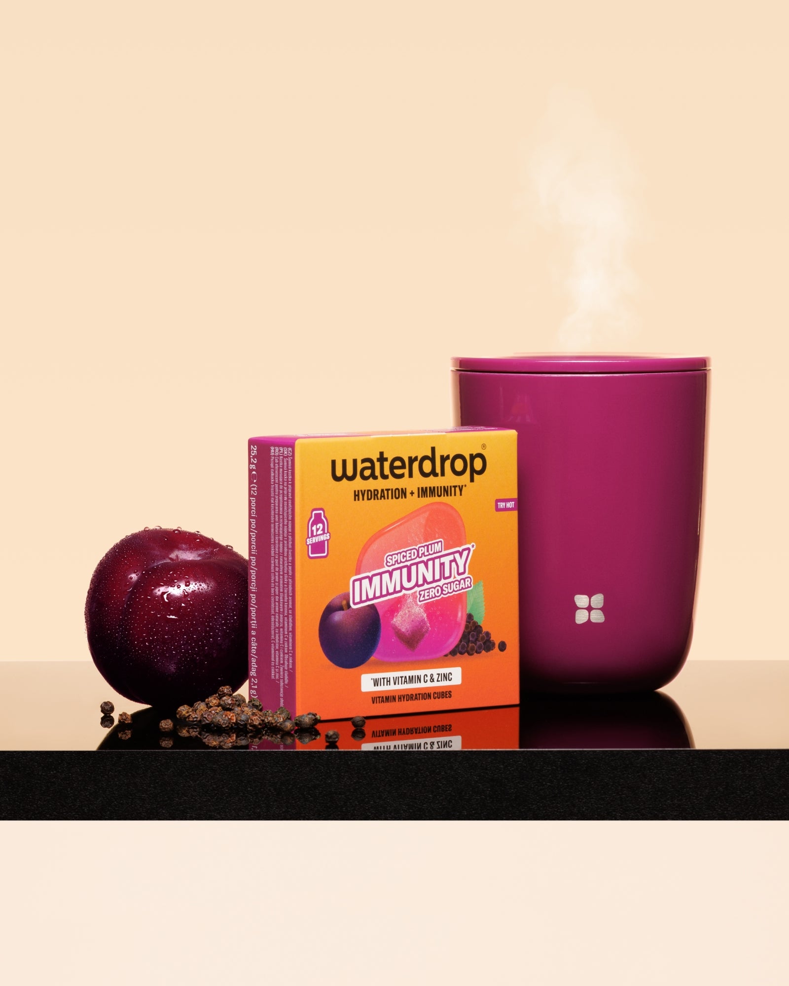 Waterdrop-Immunität-Boost-Box neben einer Pflaume und einer dampfenden rosafarbenen Tasse auf einer schwarzen Oberfläche.