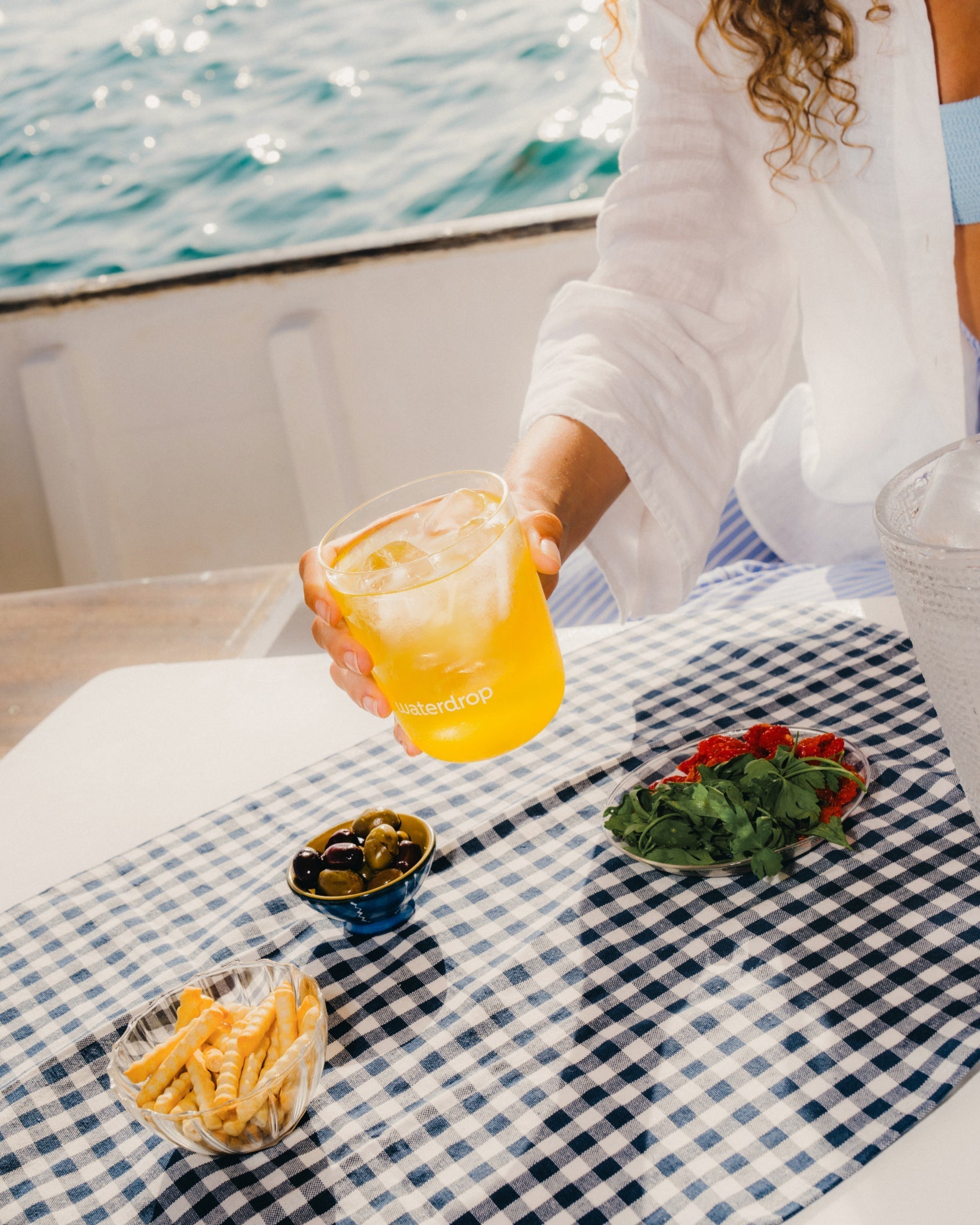 Hot & Hydrated Set auf sommerlich gedecktem Tisch mit Oliven und Drink.